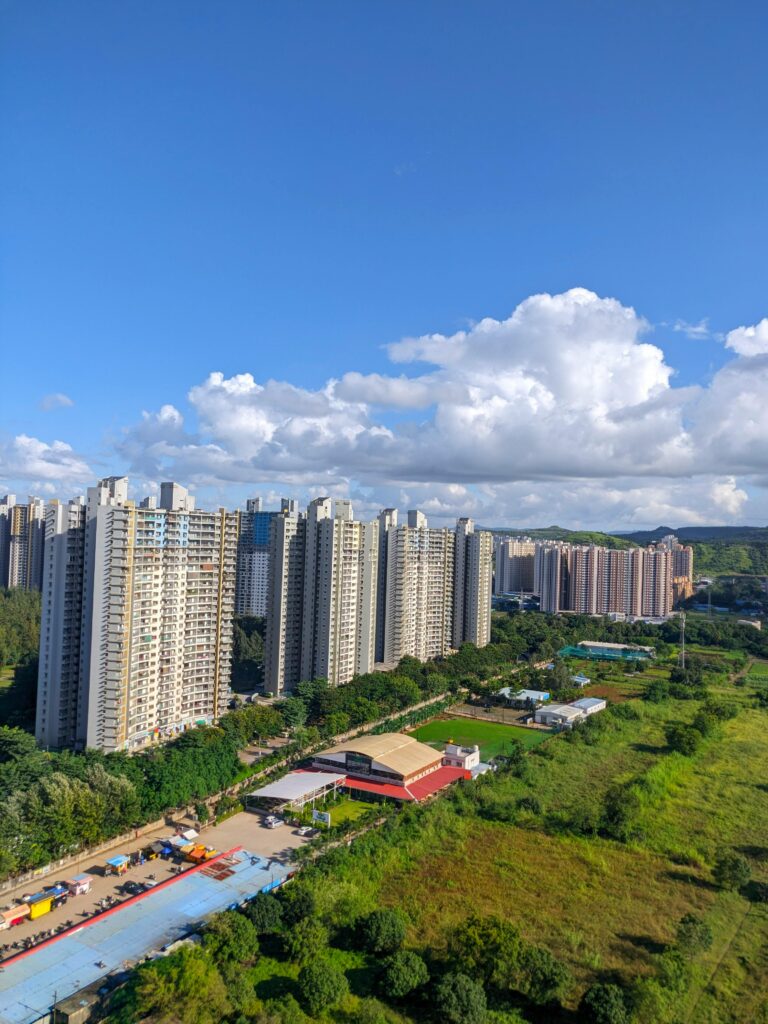pexels-photo-29285205-29285205 Aerial view of tall residential buildings in Pune, India, with lush greenery and a vibrant sky.